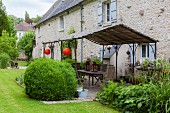 Mit Lampions dekorierter Terrassenplatz mit Metallpergola vor Naturstein-Landhaus und angelegtem Garten