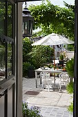 View into idyllic courtyard with greenery, vintage-style garden furniture and white parasol