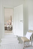 Steps and open interior door between two, white-panelled rooms; worn, antique chair in foreground