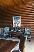 Table with drawers flanked by armchairs below painting in log-cabin-style dining room
