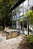 Contemporary house with glass and steel façade and weathered wooden table and bench on tiled terrace