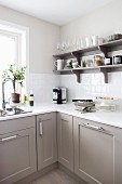 Corner of kitchen with white worksurface on grey-painted base units below colour-coordinated wall-mounted shelves