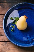 Pears poached in white wine with syrup and fresh mint in a blue ceramic bowl