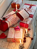 Verpackte Weihnachtsgeschenke in Rot mit kleinen Botschaften, Dekoherzen und brennende Kerzen