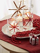 Christmas decoration – a string of red beads next to floating candles on a white dish