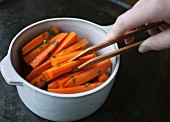 Cooked carrots being removed from a saucepan with a pair of tongs
