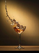 A cocktail splashing out of a glass with ice cubes