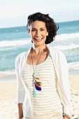 A dark-haired woman on a beach wearing a light t-shirt and jacket
