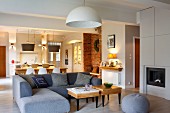 Modern, grey corner sofa and small, wooden side table in front of dining area in open-plan, rustic interior