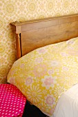 Detail of bed with wooden headboard, floral bed linen and floral wallpaper