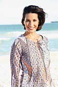 A dark-haired woman on a beach wearing a patterned blouse