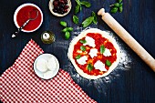 An unbaked pizza with tomatoes, mozzarella and basil