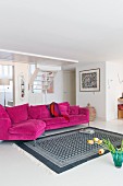 White and grey patterned rug in front of magenta couch in bright living room