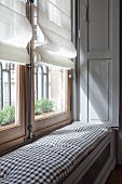 Window seat with cushion on top of radiator cover in niche of window in period apartment