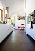 Lowdown view of a modern kitchen between the kitchen surface and built in appliances with dining area and red chairs in the background