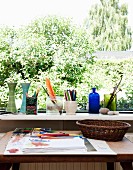 Tisch mit Malutensilien und Zeichnung vor Fenster mit Aussicht, auf Fensterbank Vasen und Behälter mit Stiften