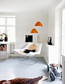 Designer Schaukelstuhl unter orangefarbener Pendelleuchten in Wohnzimmerecke, seitlich Retro Spielzeugauto auf grauem Dielenboden