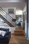 View from elegant living room to steel staircase with wooden treads; fitted kitchen with grey glossy fronts in background
