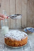 An apple and hazelnut cake being dusted with icing sugar