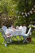 Sommer-Gartenparty mit romantisch gedecktem Tisch, gemütlich gepolsterten Gartenstühlen und nostalgischer Wimpelkette