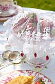 Selbstgenähte Fliegenschutzhaube aus weißem Spitzenstoff für Erdbeerschale auf romantisch gedecktem Gartentisch