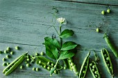 Peas with pods and a flower on a green wooden surface