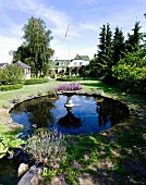 Pflanzengefäss auf Stele aus Stein im Karpfenteich in angelegtem Garten, im Hintergrund Landhaus