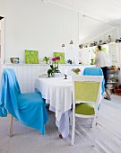 Runder Essplatz mit verschiedenen Stühlen, weiße Holzverkleidung in hellem Cottage Ambiente mit Blick in Küche