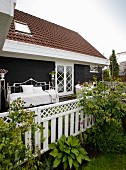 View from garden onto terrace with white, metal daybed against dark wooden wall