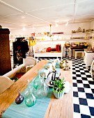 Showroom with chequered floor, collection of bottles and crockery on turquoise runner on wooden table