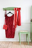 Red dress on coat hanger and scarves hung from green-painted coat rack with matching side table with curved legs