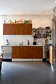 Retro kitchen with teak and stainless steel doors, various pans and cooking utensils hanging from wall-mounted shelf