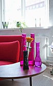 Arrangement of various vases on small retro table next to red sofa in living area