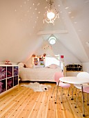 Kinderzimmer in ausgebautem Dach, seitlich Tisch mit farbigen Stühlen, im Hintergrund Bett am Fenster, Pendelleuchte mit reflektierendem Licht an Decke eines Satteldaches