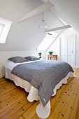 Black and white striped bedspread on double bed in white bedroom in renovated attic with wooden floor