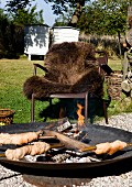 Campfire bread in fire bowl in front of outdoor armchair with brown fur blanket in garden