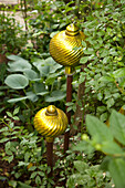 Ornate, yellow glass balls on sticks amongst plants in garden