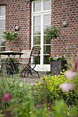 View from garden to seating area with folding chairs and table outside brick farmhouse with white, lattice French doors