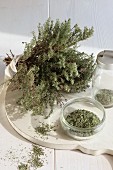 A bundle of dried thyme with thyme leaves in a a glass bowl and a spice jar in front of it