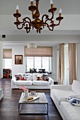 Bright, open-plan interior with chandelier in front of purist coffee table and white sofas