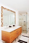 Modern bathroom with washstand, wooden base cabinets, mirror with mosaic frame and glass shower cubicle
