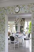 Dining area with opulent chandelier above antique-style white dining table and chairs