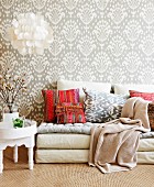 Seating area with colourful cushions, grey peacock-patterned wallpaper, capiz shell lampshade and white tray table providing Oriental accents