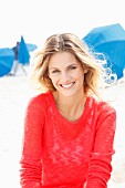 A young blonde woman on a beach wearing a transparent red knitted jumper