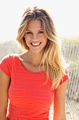 Junge blonde Frau in lachsfarbenem Shirt am Strand