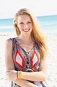 A young blonde woman on a beach wearing an ethnic patterned summer dress