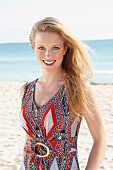 A young blonde woman on a beach wearing an ethnic patterned summer dress