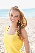 A young blonde woman on a beach wearing a yellow top