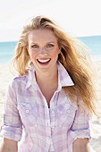 A young blonde woman on the beach wearing a purple and white checked blouse