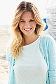 A young blonde woman on a beach wearing a light shirt and a light-blue cardigan